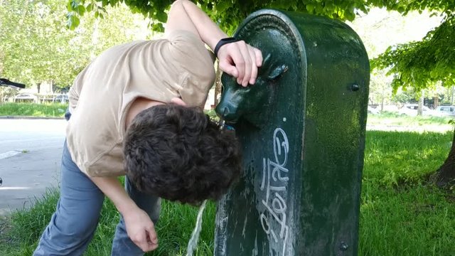 A young Caucasian boy drinks from a public drinking fountain in Turin, Italy. The fountain represents the head of a bull, symbol of the city. 30 fps
