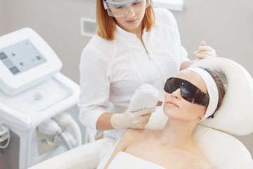 Professional cosmetologist doing an ultrasonic peeling to a client woman lying on a couch. Skin cleansing concept and modern rejuvenation technologies