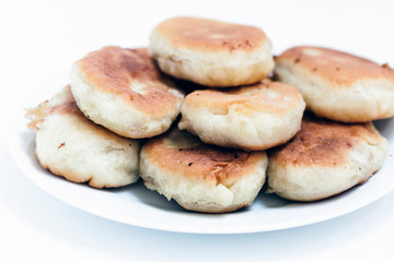 Traditional homemade fried patties or pies made of yeast dough in a rustic style on white plate.