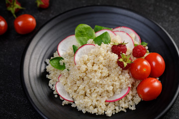 Quinoa salad with vegetables, raspberry and tomatoes on the black table. Super food for healthy and concept of balanced diet