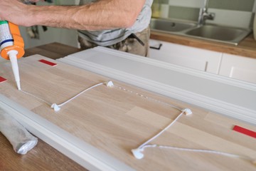 Carpenter male using construction glue when working with wooden white painted board, closeup,...