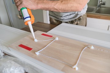 Carpenter male using construction glue when working with wooden white painted board, closeup,...
