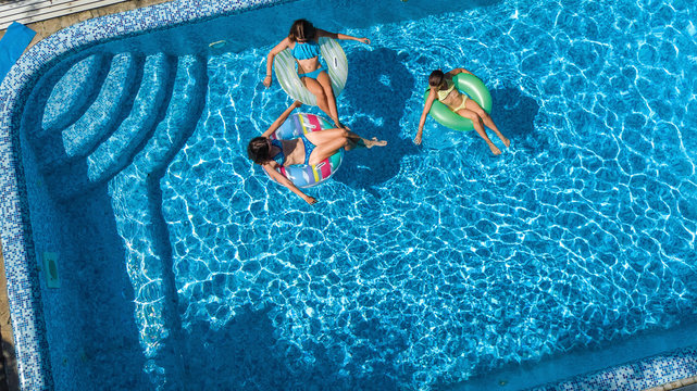 Family in swimming pool aerial drone view from above, happy mother and kids swim on inflatable ring donuts and have fun in water on family vacation, tropical holidays on resort