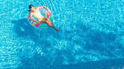 Acrive girl in swimming pool aerial top view from above, kid swims on inflatable ring donut , child has fun in blue water on family vacation resort