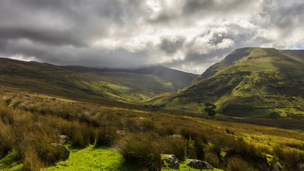 An exciting colorful cloudy sky with a few rays of sunshine in the lush green mountains of snowdonia in the north of Wales.