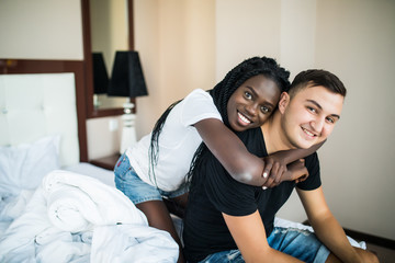 Beautiful young african woman embracing boyfriend from behind in bedroom. Mixed race couple