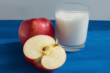 Glass of milk and red apple on blue background