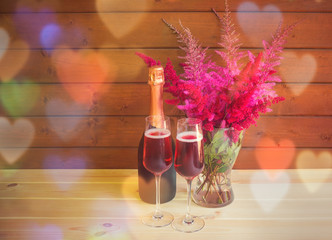 Two glasses of rose champagne, bottle of rose champagne and astilbe flowers on wooden table.
