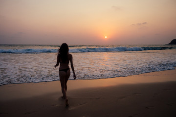 young woman in sexy swimming suit black thong in sea wawes having fun at sunset Goa beach India ocean