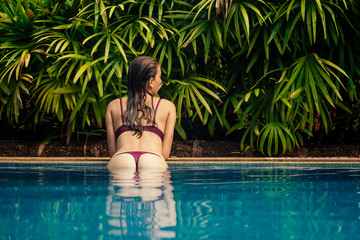 rich brunette woman in swimmingpool on sea beach with palm trees luxury vacation hotel . spf sunscreen protection buttocks and thighs copyspace - obrazy, fototapety, plakaty
