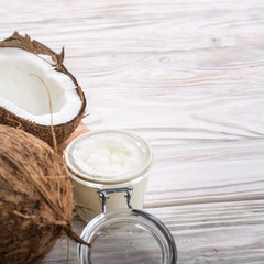 Coconut oil in airtight glass jar and shell pieces on white wooden table closeup