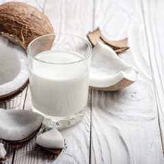 Drinking glass of milk or yogurt on blue napkin on white wooden table with coconut aside
