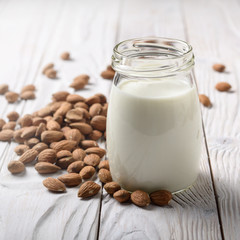 Milk or yogurt in mason jar on white wooden table with almonds aside