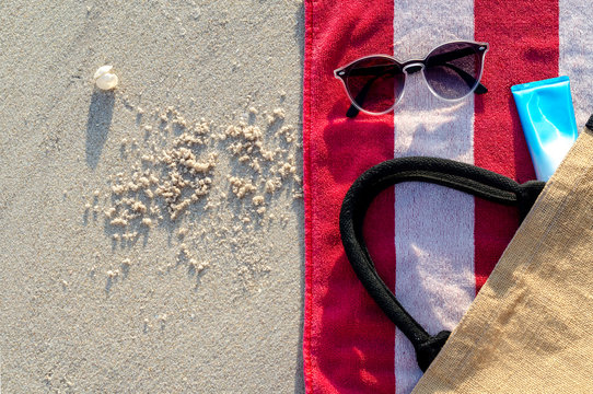 Sunglasses with sunscreen lotion and bag on red towel put on sand for a trip on summer season at the beach.