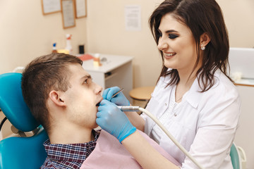 Fototapeta premium Picture of young female dentist in white coat working with male patient in the dental room