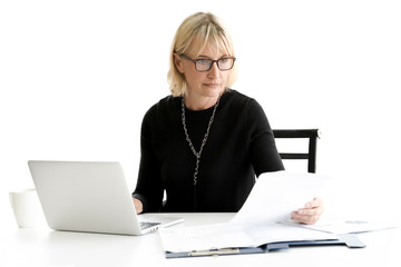 Serious mature businesswoman using laptop and looking document while working at office on white background