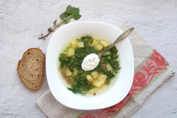Green summer soup with nettle meat and potatoes with bread on a table napkin on a grey concrete background