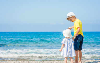 Brother and little sister standing holding hands on the beach on summer holidays. concept of summer family vacation. Space for text