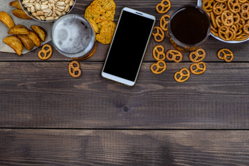 Varied snacks with beer and smartpnone on dark wooden background. Internet delivery concept. Top view. Empty space for text