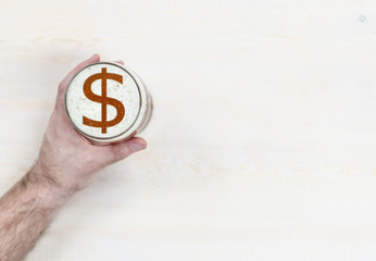 man's hand holds a mug of beer with sign of a  dollar usa  on a beer foam. Top view. Space for text