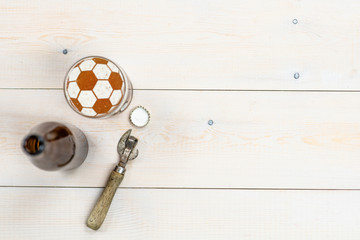 Mug of craft beer with a soccer ball on a beer foam and bottle with retro opener on light wooden...