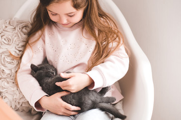 Smiling child girl 3-4 year old holding sleeping kitten in room close up. Friendship. Childhood.