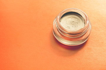 Creamy eye shadow with a metallic effect in a glass jar isolated on orange background.