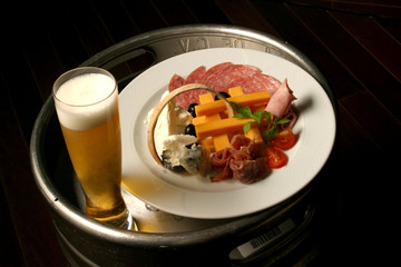 Cheese plate, serrano ham, salami and goat cheese accompanied by beer.