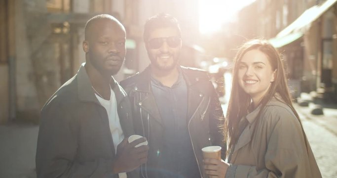 Happy smiling multirace people holding coffee cups on the city street against sunset, carefree youth freedom concept