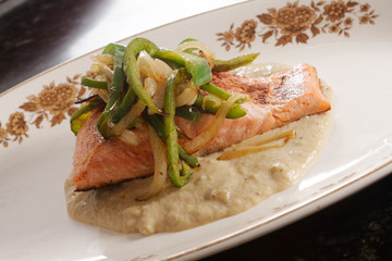 Roasted salmon fillet with almond sauce served with peppers and caramelized onions.