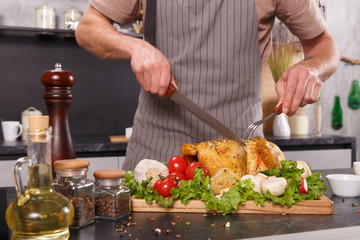 Hands of chief man cuting baked chicken with vegetables