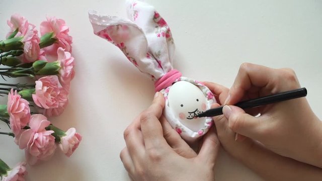 Women's and children's hands hold chicken egg decorated for Easter bunny in hands, paint rabbit's face with marker. Handmade Easter design
