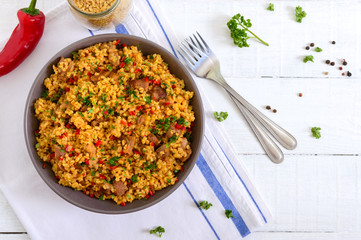 Delicious bulgur with vegetables, meat and greens on a white wooden table. Dietary menu. Proper nutrition. Top view.