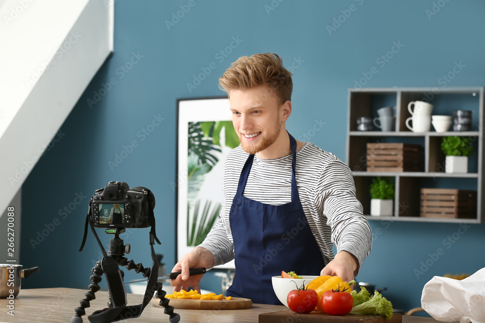 Wall mural Young male food blogger recording video in kitchen