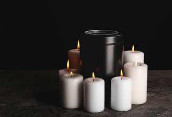 Fototapeta na wymiar Mortuary urn with burning candles on table against dark background