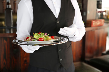 Young male waiter with salad in restaurant, closeup