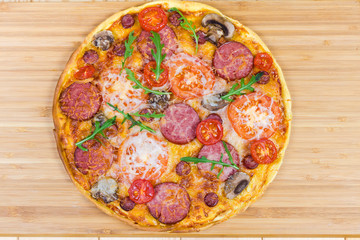 Cooked round pizza with sausages and mushrooms on cutting board