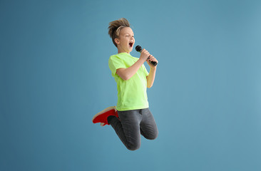 Jumping little boy with microphone on color background