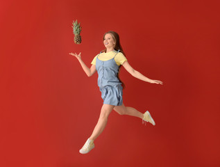 Jumping woman with pineapple on color background