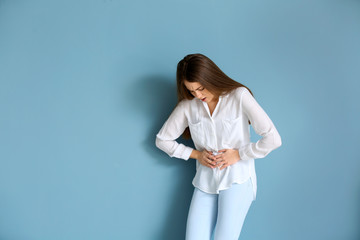 Young woman suffering from abdominal pain on color background