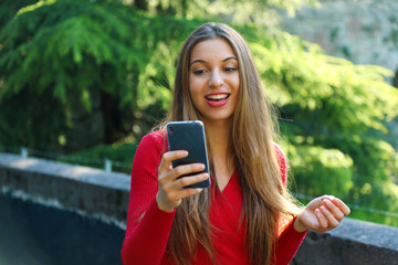 Happy beautiful young woman using smart phone app outdoor