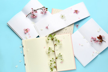 Beautiful blossoming branches and open notebooks on color background