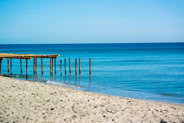Piles and a fragment of an old wooden pier protrude from the sea water near the sandy shore