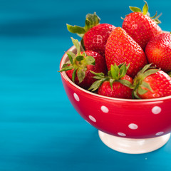 colorful ripe strawberries in a bright bowl on a blue background
