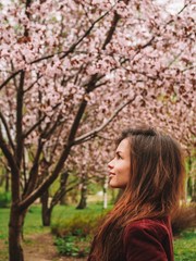 Brunette girl with long hair in a red jacket is surrounded by pink Sakura flowers