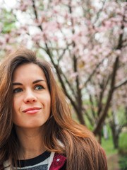 Fototapeta premium Brunette girl with long hair in a red jacket is surrounded by pink Sakura flowers