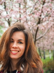 Brunette girl with long hair in a red jacket is surrounded by pink Sakura flowers