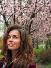 Naklejka premium Brunette girl with long hair in a red jacket is surrounded by pink Sakura flowers
