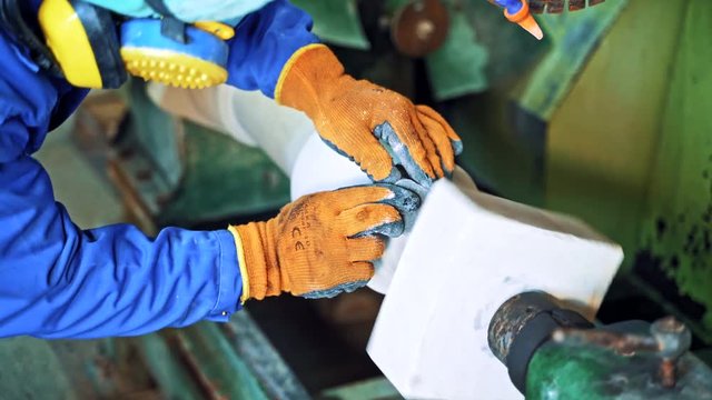 Man's hands in protective gloves polishing stone by grinder. Industrial tool is grinding rock in the factory. Hard work. Close-up.