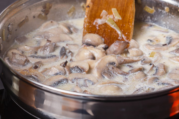 young woman in a gray apron adds milk to mushroom sauce